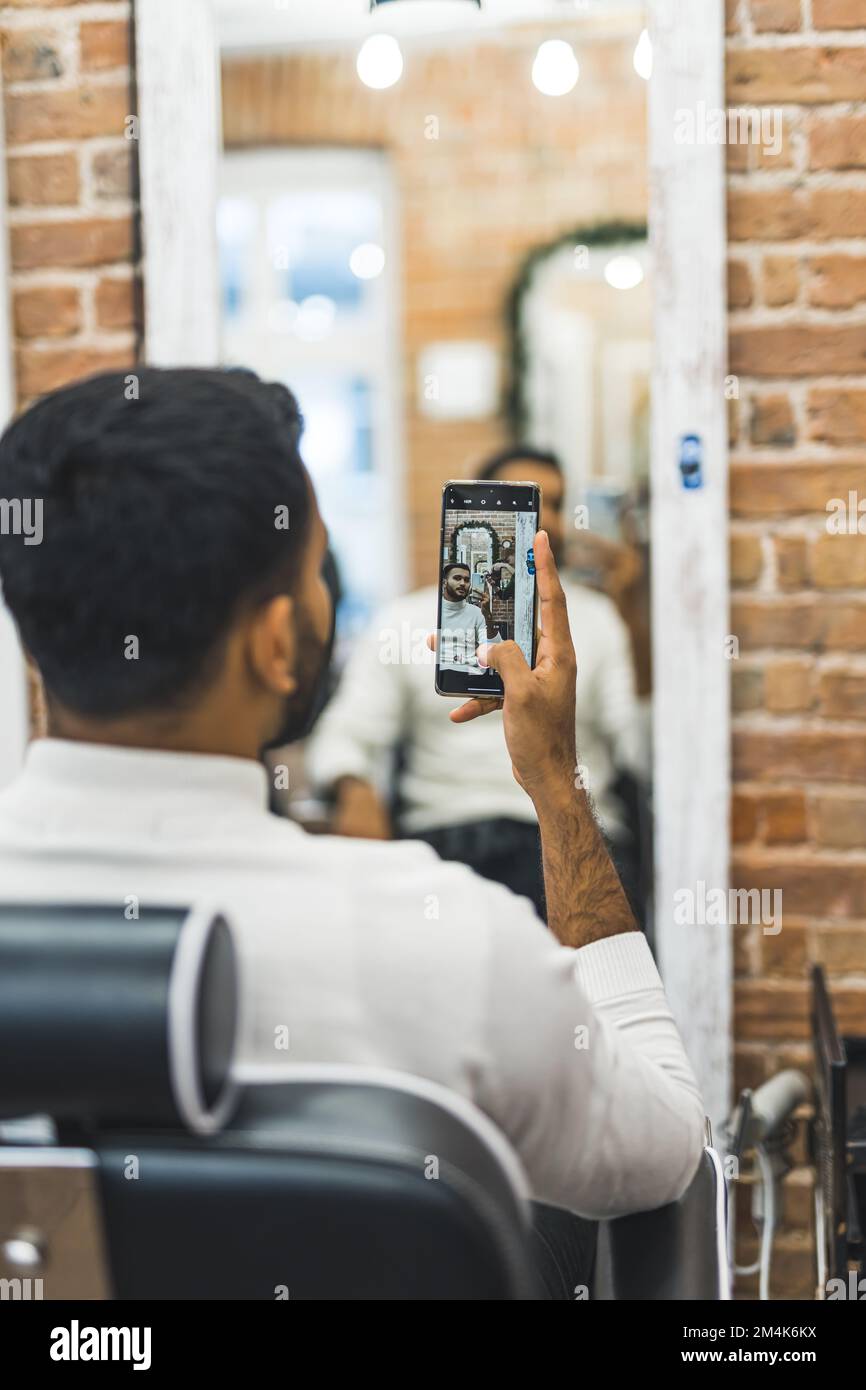 vue arrière d'un homme prenant un selfie miroir au barbershop, prise verticale. Photo de haute qualité Banque D'Images