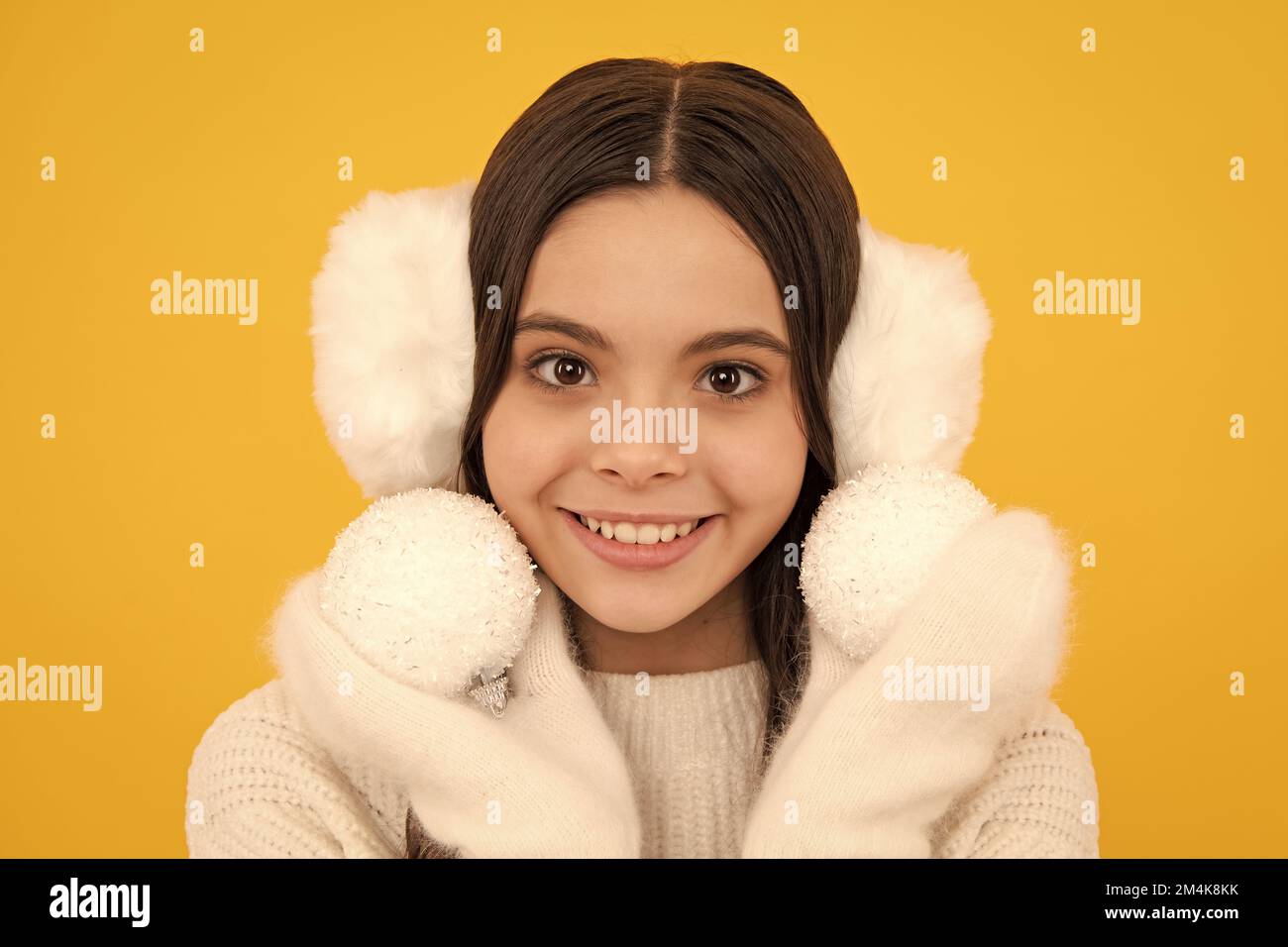 Portrait de l'adolescent heureux fille porte chandail et gants tricotés, tenir boule de noël, pose sur fond jaune isolé. Banque D'Images