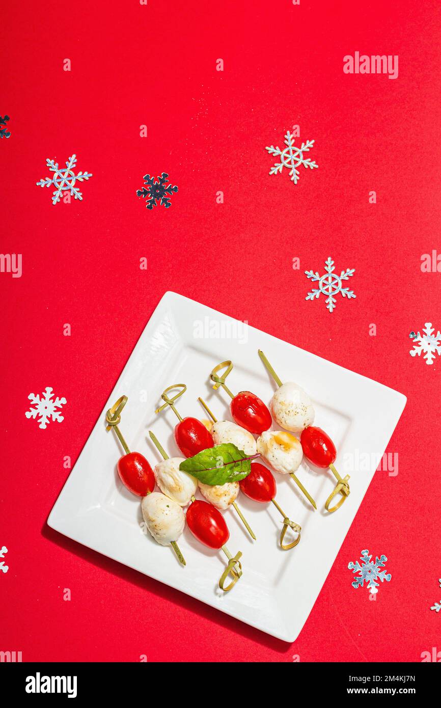 Hors-d'œuvre italien traditionnel dans le style de Noël. Mozzarella et tomates cerises sur brochettes. Design nouvel an, lumière dure moderne, ombre foncée, bac rouge Banque D'Images