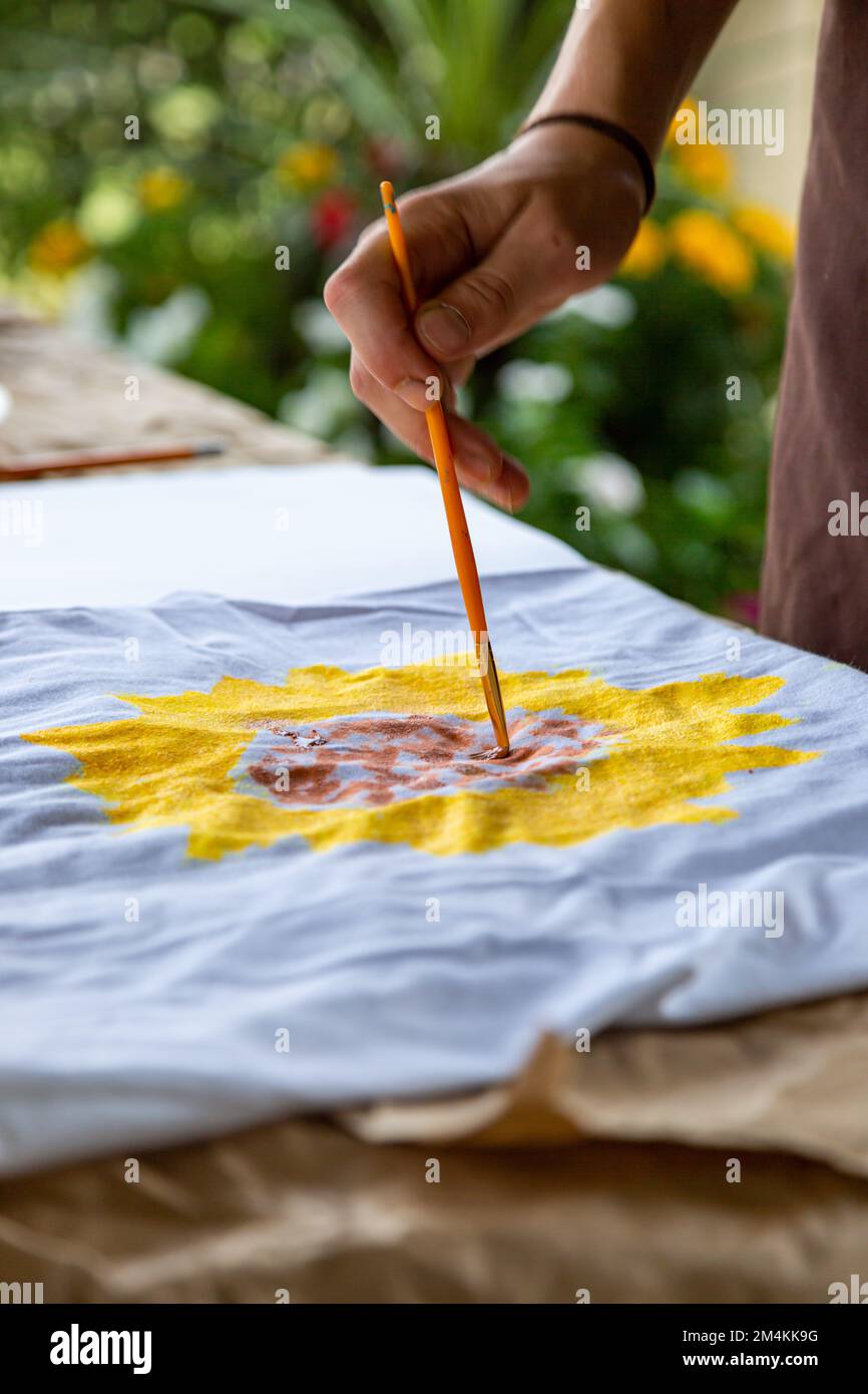 Un artiste peint une photo d'un tournesol sur un t-shirt blanc. Banque D'Images
