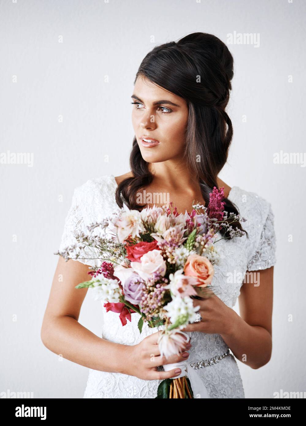 Je suis en train du faire. Studio portrait d'une jeune mariée tenant un bouquet de fleurs sur fond gris. Banque D'Images