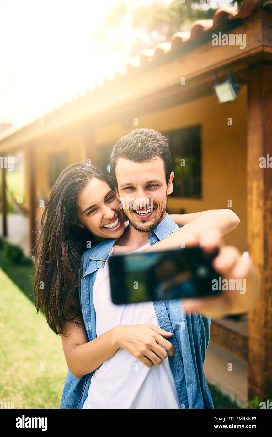 Immortalisez ces moments uniques. un jeune couple affectueux prenant des selfies dehors avec leur maison dans le fond. Banque D'Images