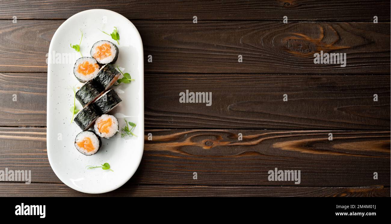 Petits pains Maki avec saumon et fromage sur plaque sur fond de bois. Menu sushi. Concept alimentaire japonais. Vue du dessus. Bannière Banque D'Images