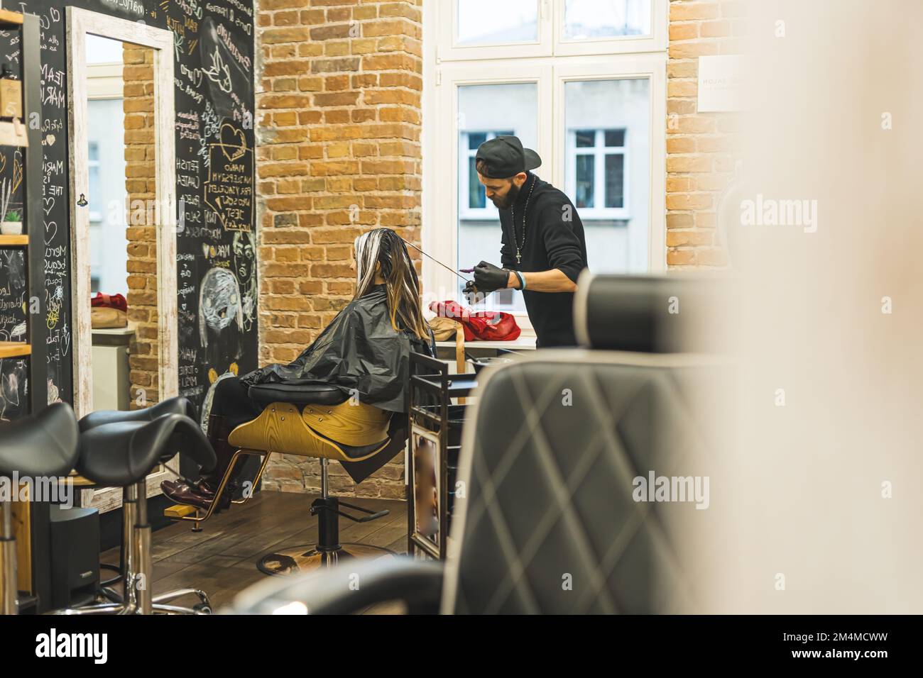 Coiffeur au travail. Cline avec de longs cheveux assis sur une chaise au salon de coiffure. Prise de vue en intérieur sur toute la longueur. Intérieur de salon de coiffure. Photo de haute qualité Banque D'Images