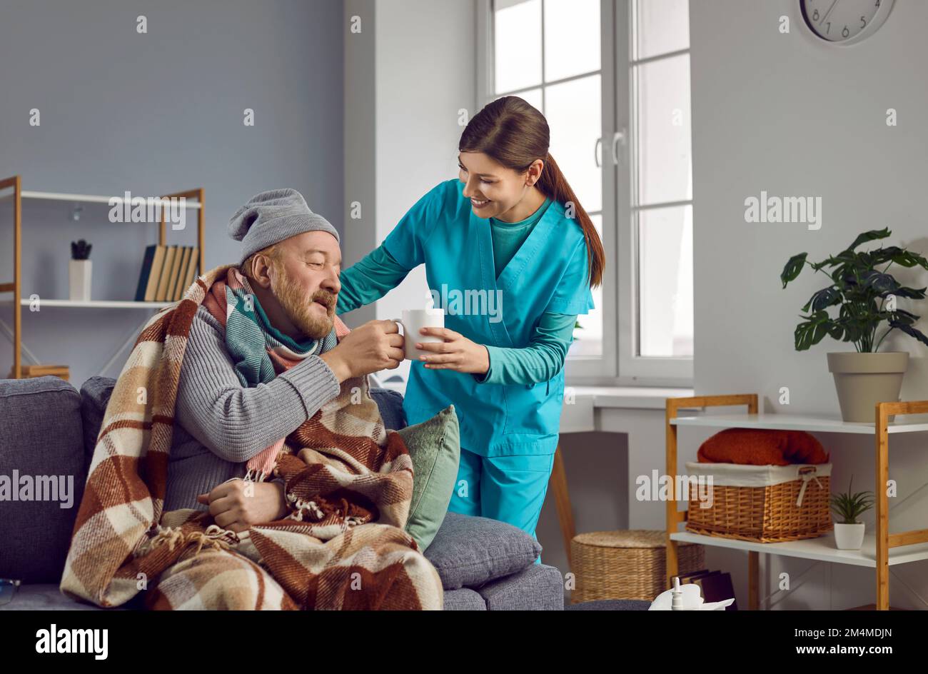 Soignant donnant une tasse de thé à un homme âgé congelé. Service de maison de soins infirmiers et soutien aux patients. Banque D'Images