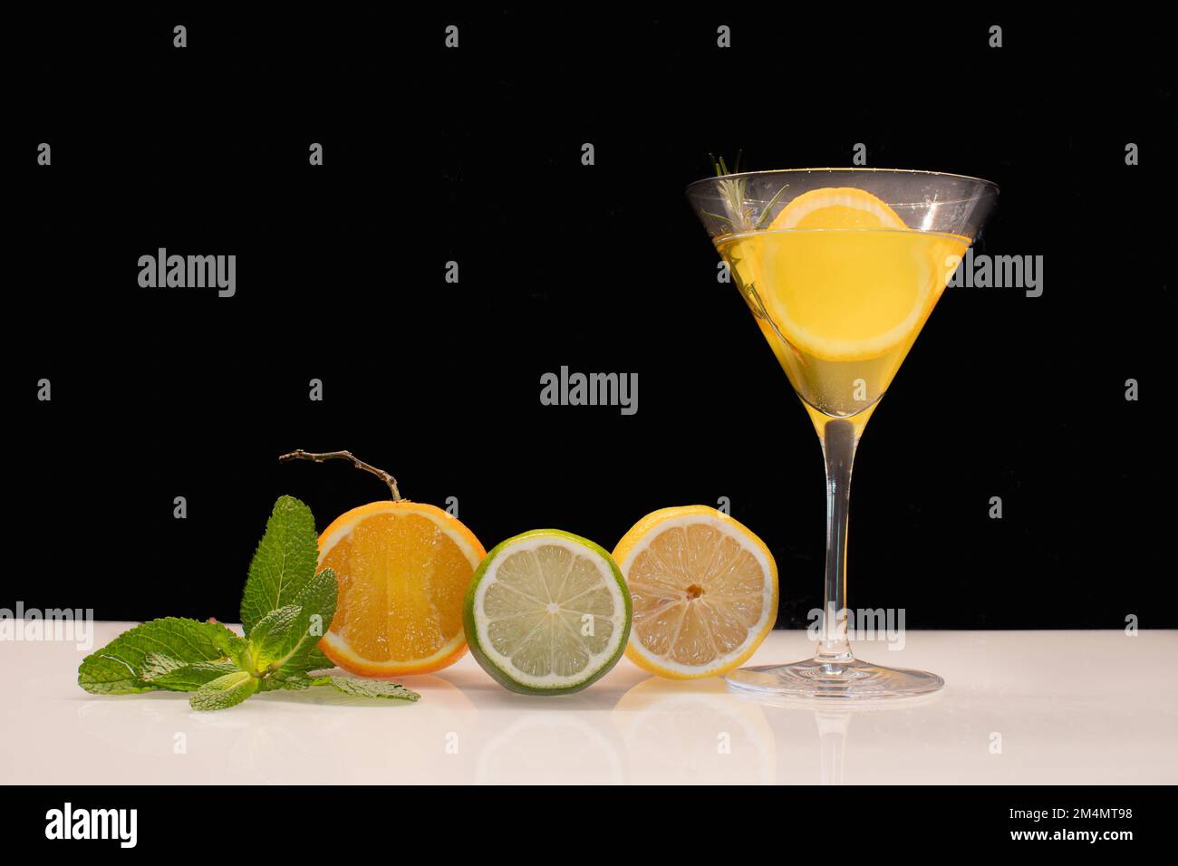 Verre à cocktail jaune avec fruits sur fond noir. Banque D'Images