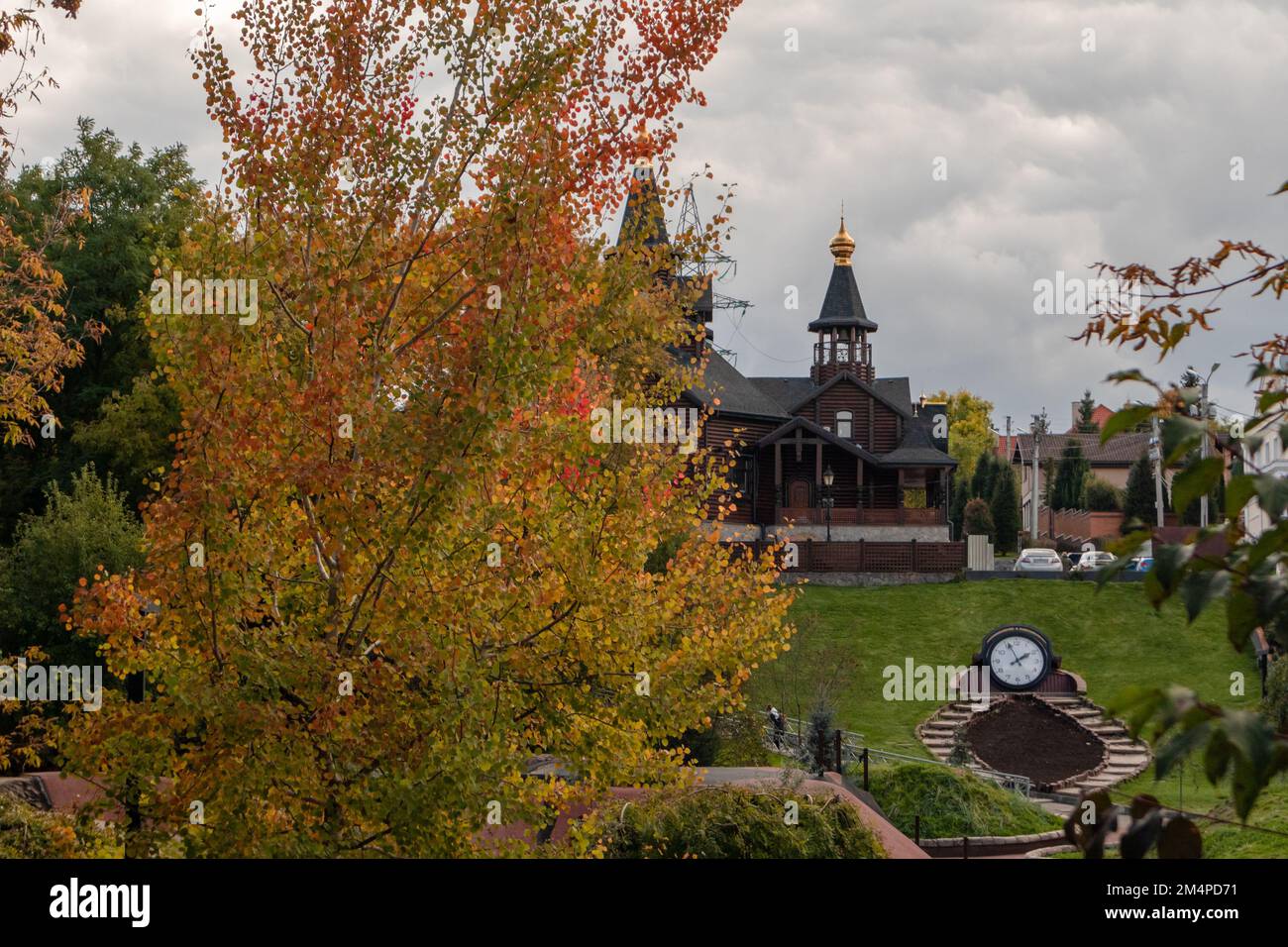 Église en bois avec dôme doré sur ciel gris nuageux derrière l'arbre coloré d'automne. Détails architecturaux dans le parc de loisirs de la ville de Kharkiv Banque D'Images