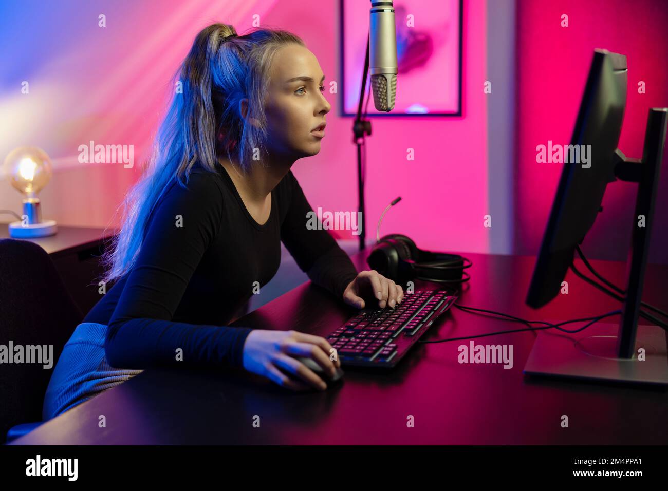 Focalisé Blond E-sport Gamer Girl avec casque jouer en ligne jeu vidéo sur PC Banque D'Images