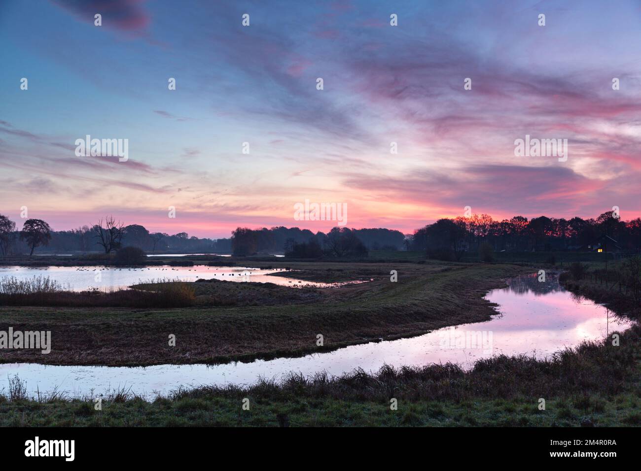 Le soleil levant baigne la rivière, les arbres, le ciel et les nuages dans une lumière rouge. Banque D'Images