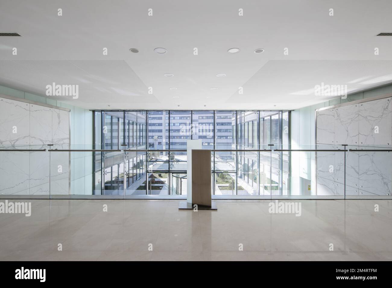 Atrium d'un immeuble de bureaux avec murs carrelés de marbre vert, sol en marbre crème, vue depuis une fenêtre en mezzanine avec balustrade en verre Banque D'Images