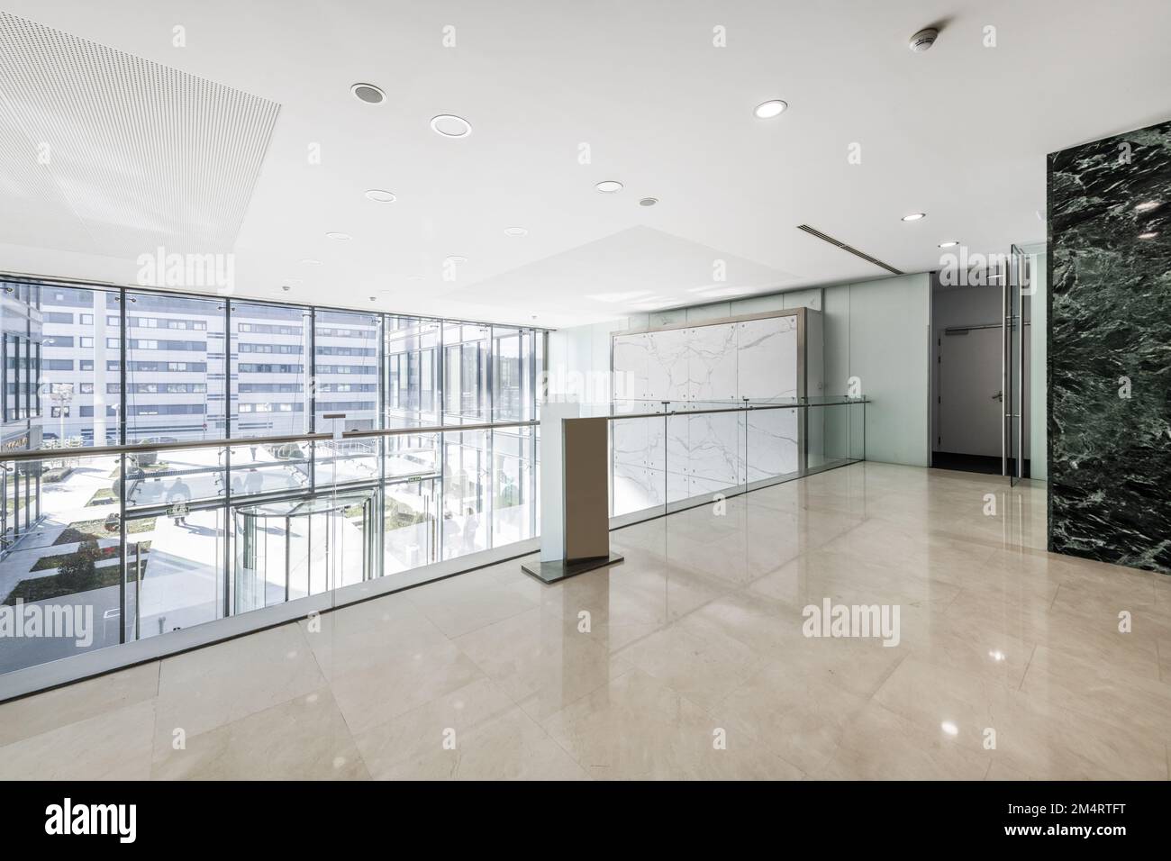 Atrium d'un immeuble de bureaux avec murs carrelés de marbre vert, sol en marbre crème, vue depuis une grande fenêtre mezzanine avec une rambarde en verre et un revolv Banque D'Images