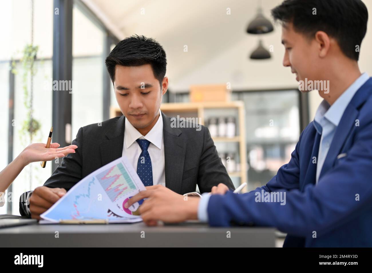 Homme d'affaires ou directeur général asiatique concentré et intelligent qui vérifie le rapport final, en collaboration avec son équipe au bureau. Banque D'Images