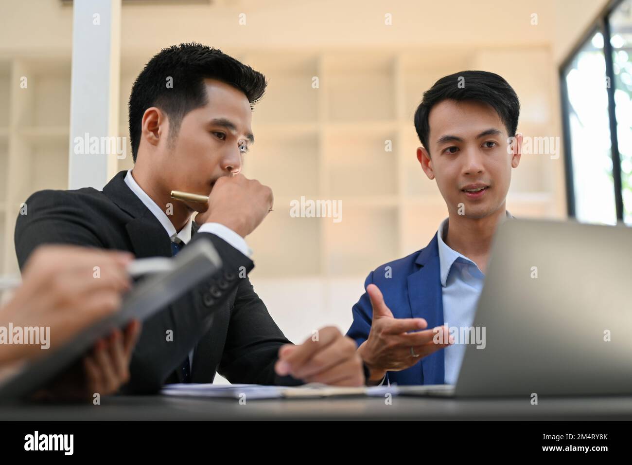 Deux hommes d'affaires asiatiques du millénaire, concentrés et intelligents, discutent, planifient et travaillent ensemble sur leur projet. Banque D'Images