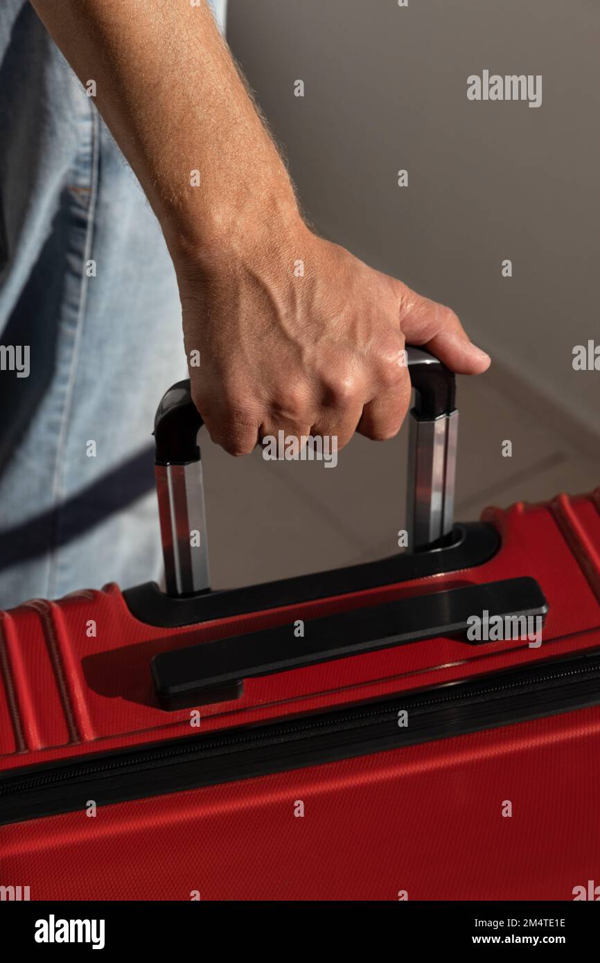 la main invisible de l'homme tient la poignée d'une valise rouge.cadre vertical Banque D'Images