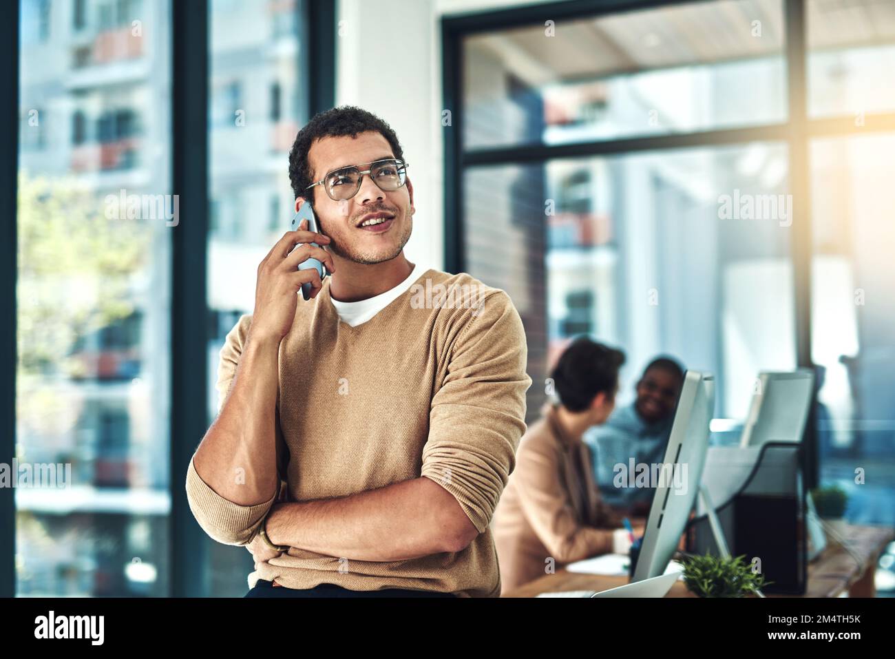 Les entreprises appellent. un concepteur parlant sur son téléphone avec ses collègues brouillé en arrière-plan. Banque D'Images