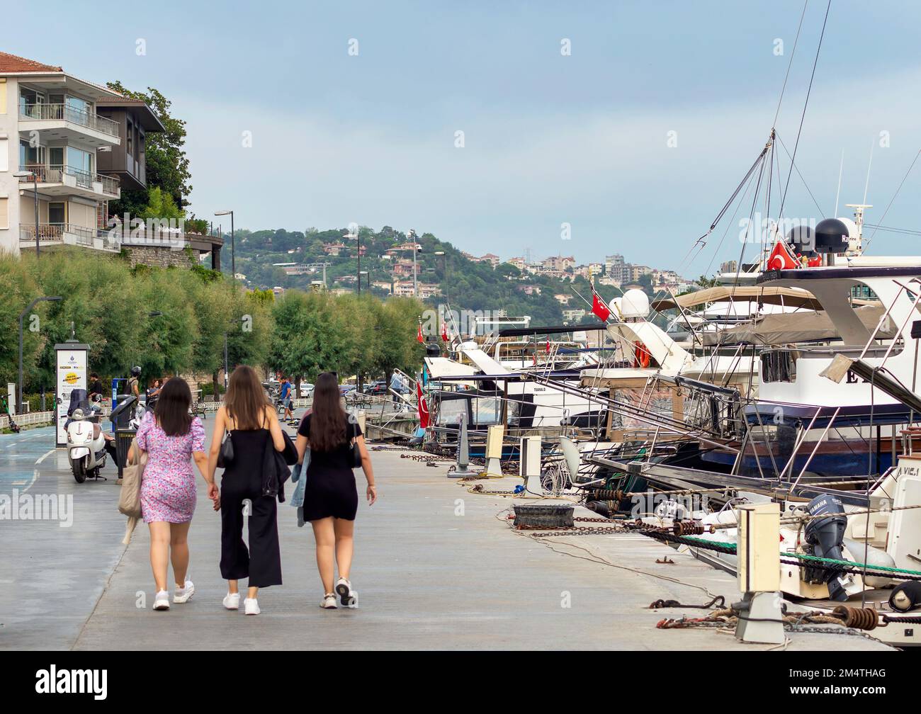 Istanbul, Turquie - 31 août 2022: Piétons marchant sur le côté à pied par le détroit du Bosphore entre les quartiers de Bebek et Hisari, à côté des bateaux à moteur et yachts amarrés, contre le ciel bleu par jour ensoleillé Banque D'Images