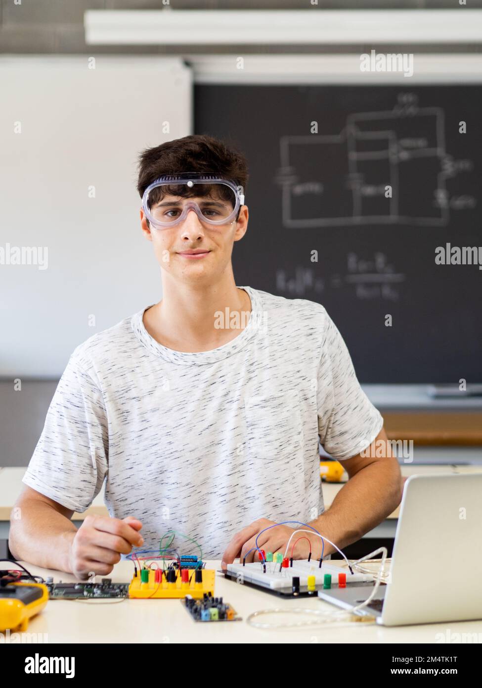 Jeune étudiant en technologie de sexe masculin regardant un appareil photo avec des lunettes de protection en classe électronique Banque D'Images
