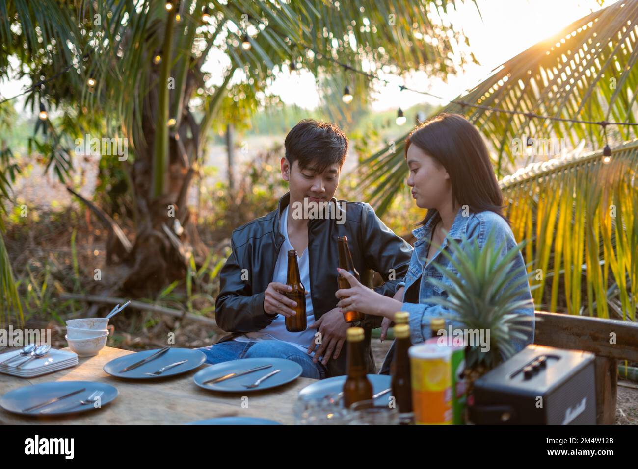 Un jeune couple asiatique se fait griller avec de la bière lors d'une fête au jardin de noix de coco Banque D'Images