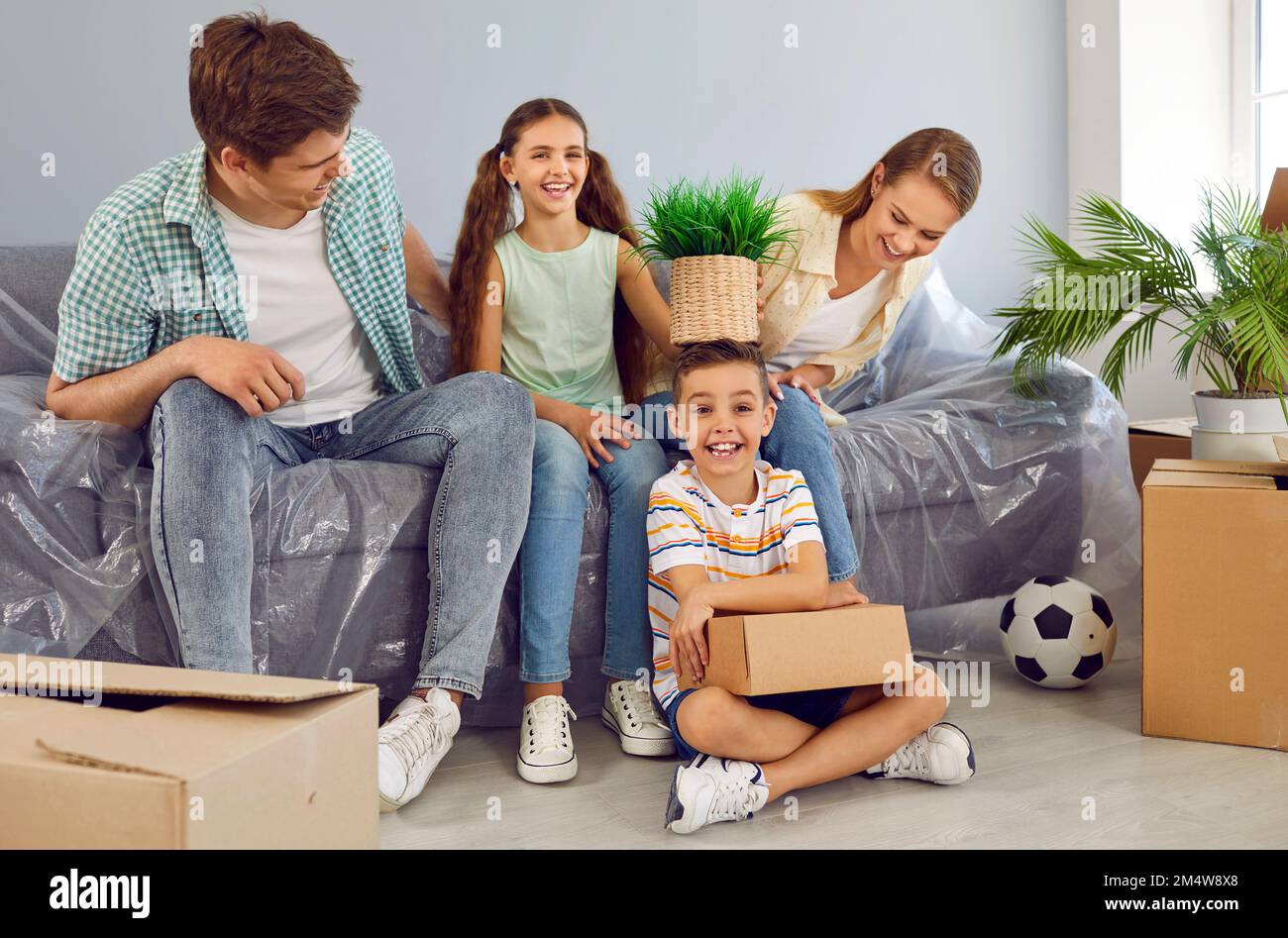 Une famille heureuse avec deux enfants assis sur un canapé se déplaçant dans une nouvelle maison d'appartement moderne parmi des boîtes. Banque D'Images