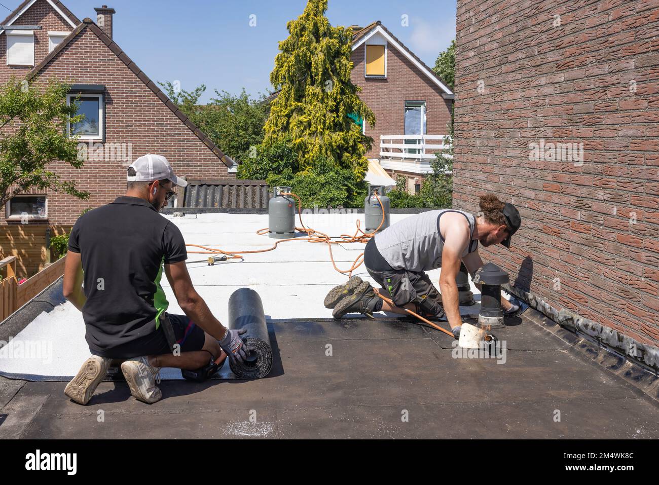 Urk, pays-Bas - 23 juin 2022: Ouvriers à toit plat préparant des rouleaux de nouveau feutre ou bitume blanc de toiture Banque D'Images