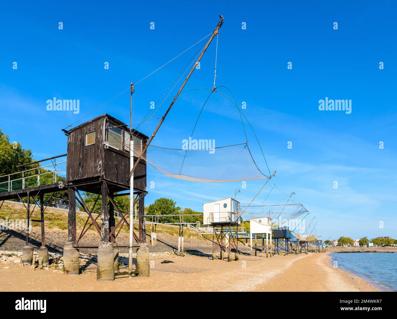Cabines de pêche avec un grand filet de remontée mécanique carré appelé 'carrelet' aligné sur la plage de Saint-Nazaire, en France, à marée basse lors d'une journée ensoleillée d'été. Banque D'Images