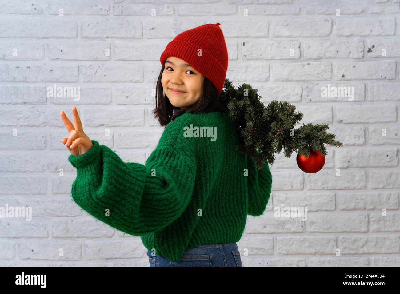 Fille souriante avec arbre de Noël signe de paix Banque D'Images