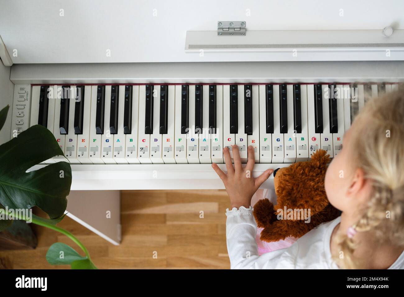 Fille avec ours en peluche apprenant le piano à la maison Banque D'Images