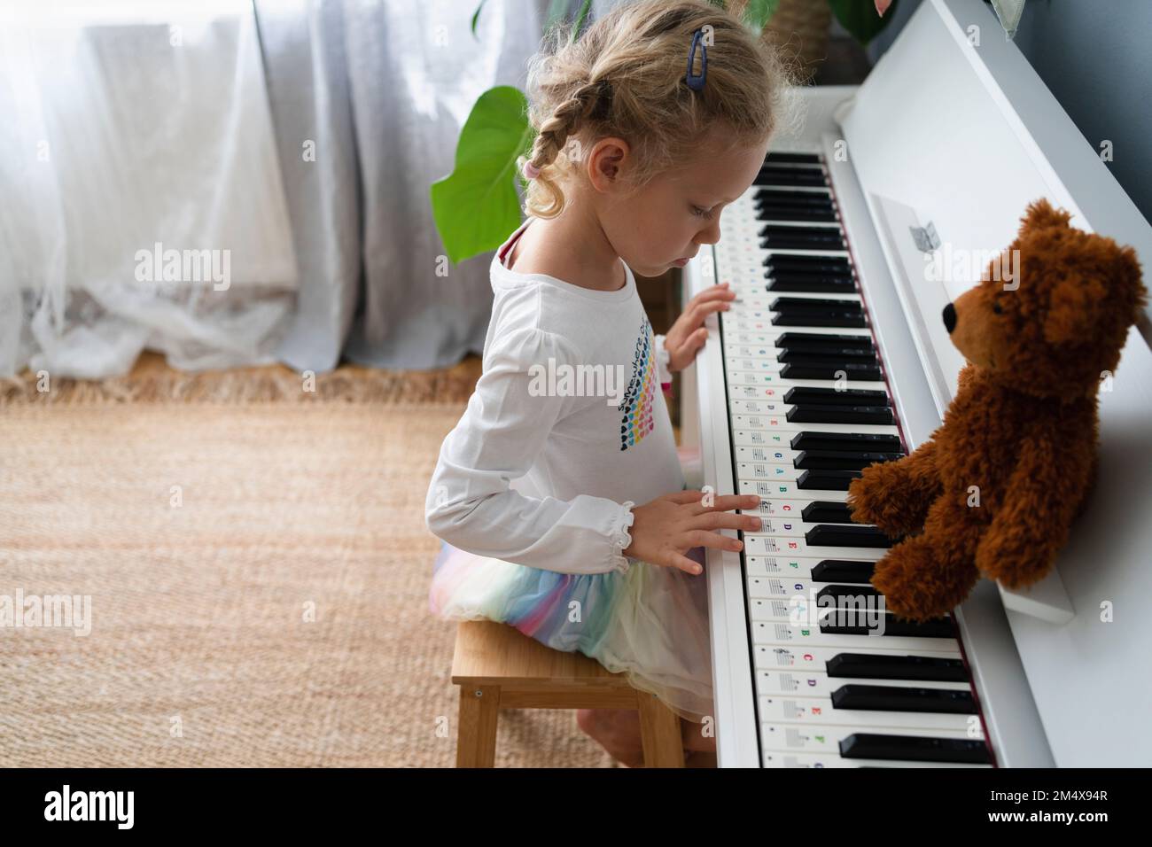 Fille apprenant à jouer du piano avec l'ours en peluche à la maison Banque D'Images