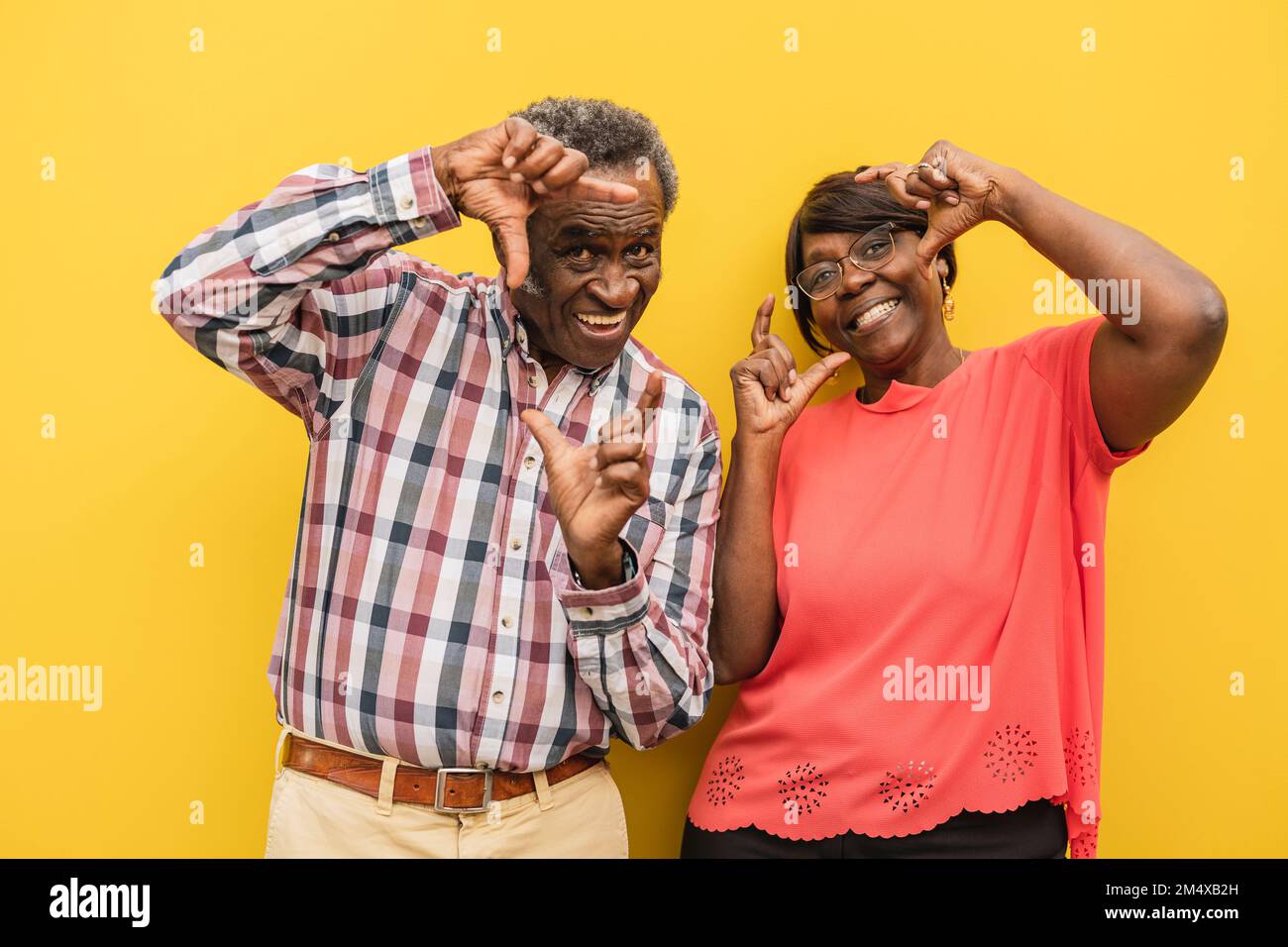 Couple senior heureux faisant des cadres de doigt sur fond jaune Banque D'Images