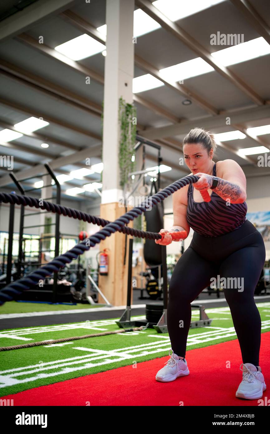 Femme déterminée s'exerçant avec des cordes de combat dans la salle de gym Banque D'Images
