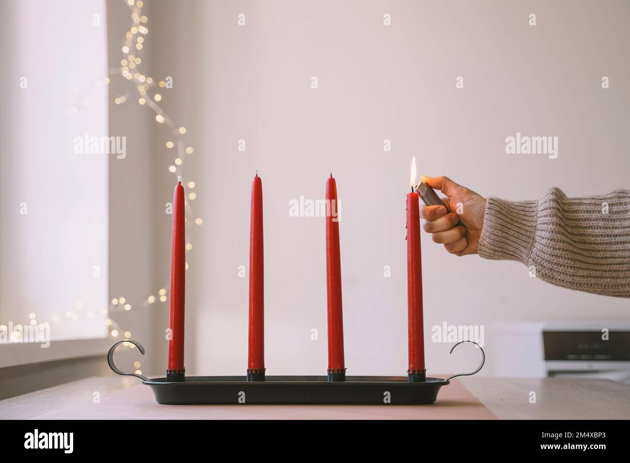 Femme brûlant une bougie rouge de l'Avent avec un briquet à la maison Banque D'Images