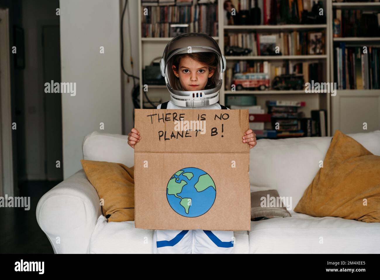 Fille portant un costume d'espace tenant une bannière avec message et dessin de planète à la maison Banque D'Images