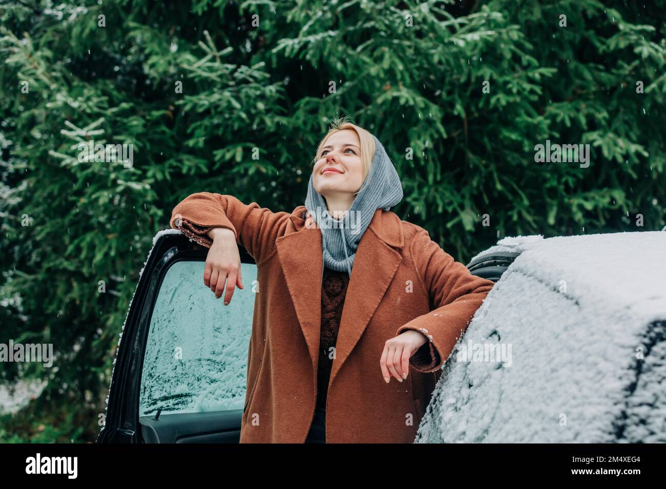 Femme souriante en voiture couverte de neige en hiver Banque D'Images