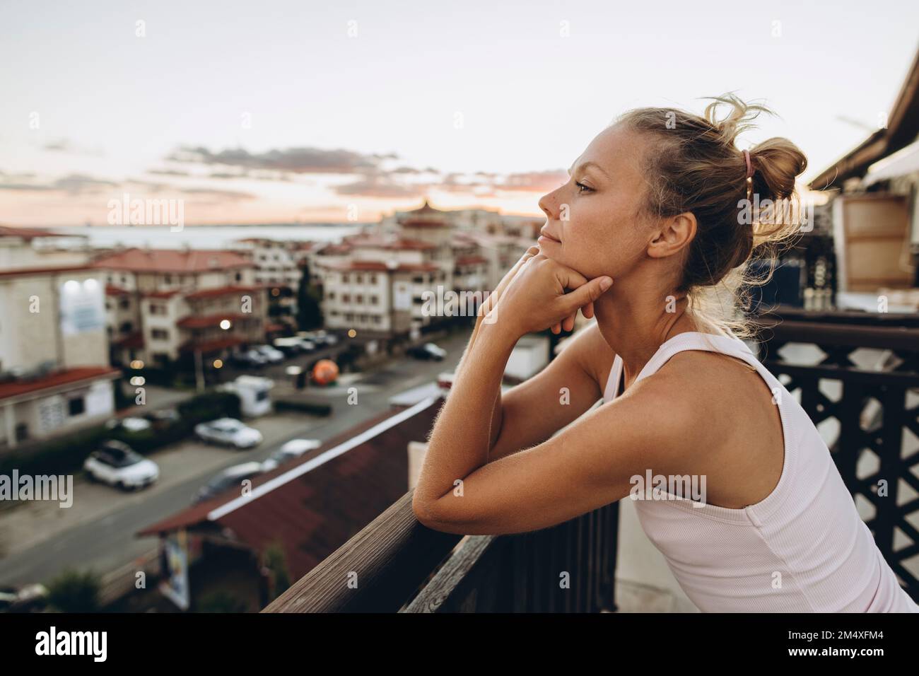 Femme s'inclinant sur la rampe de la terrasse du toit au coucher du soleil en regardant la vue Banque D'Images