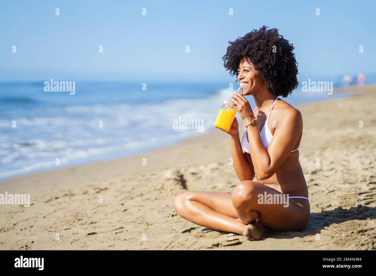 Bonne femme buvant du jus d'orange à la plage en été Banque D'Images