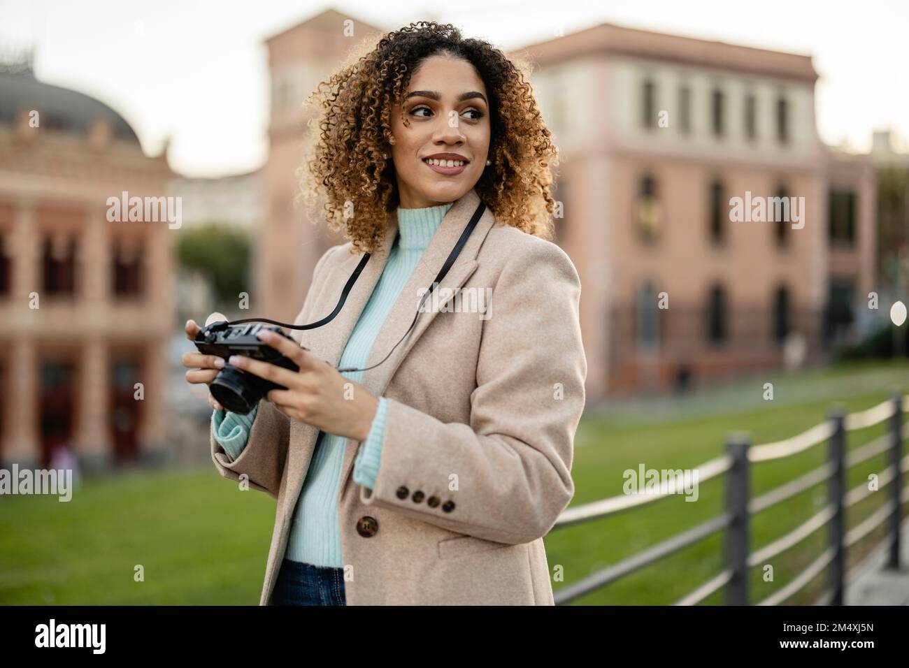 Femme souriante tenant l'appareil photo devant le bâtiment Banque D'Images