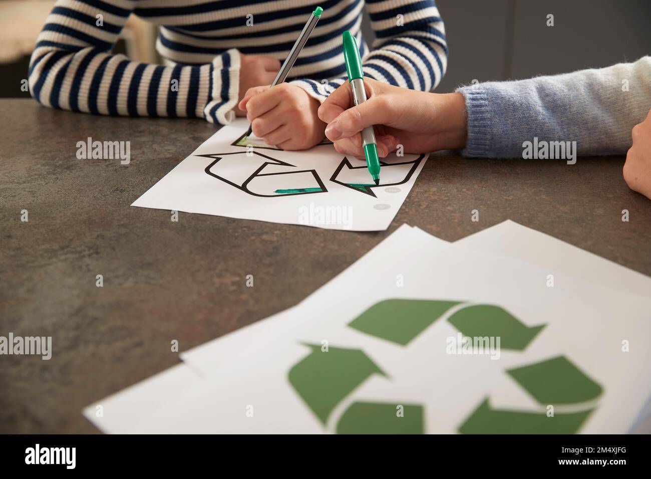 Mains de filles colorant le symbole de recyclage avec un stylo à la table Banque D'Images