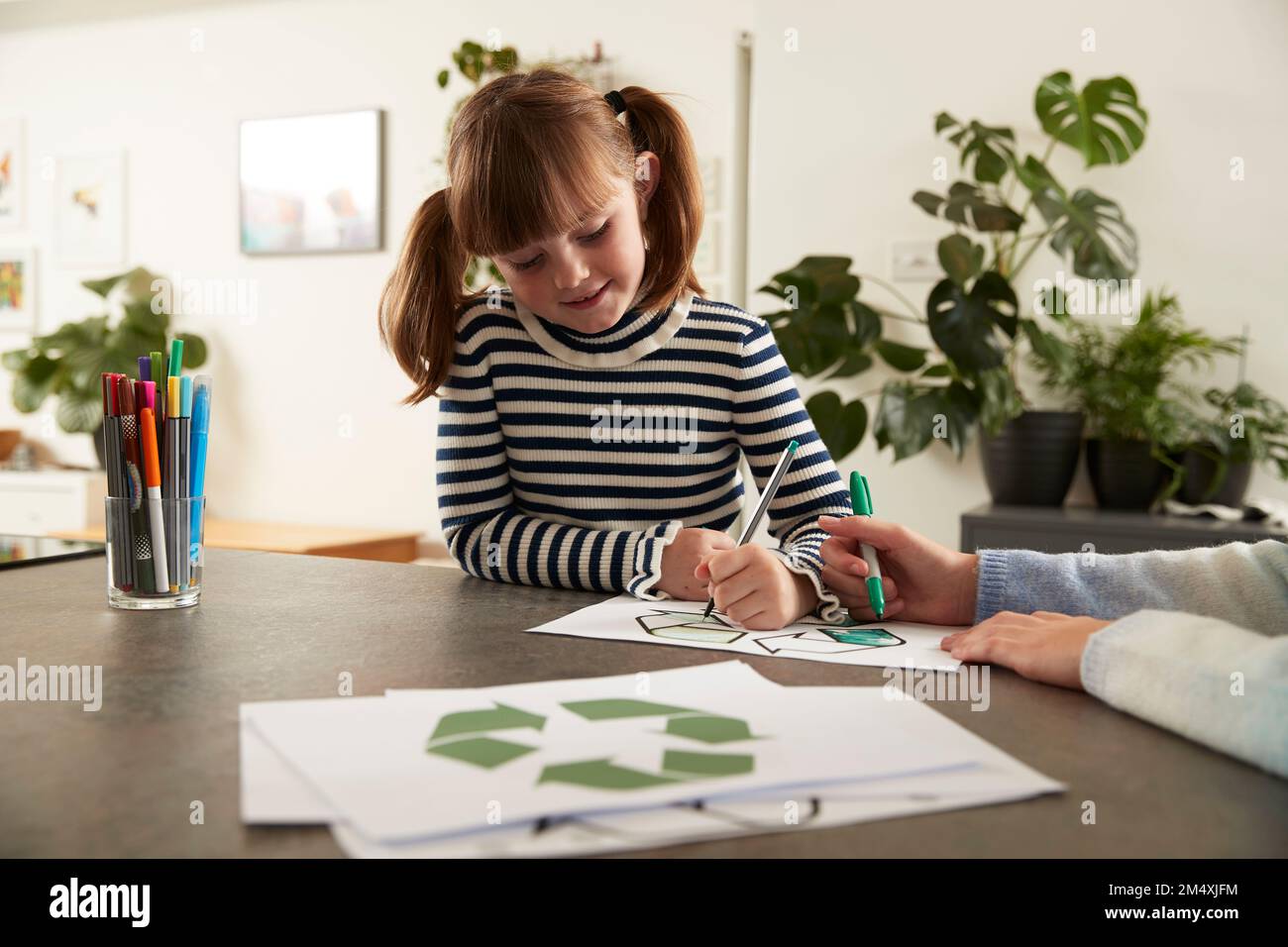 Une jolie fille souriante avec un symbole de recyclage de coloration de sœur et un stylo à la maison Banque D'Images