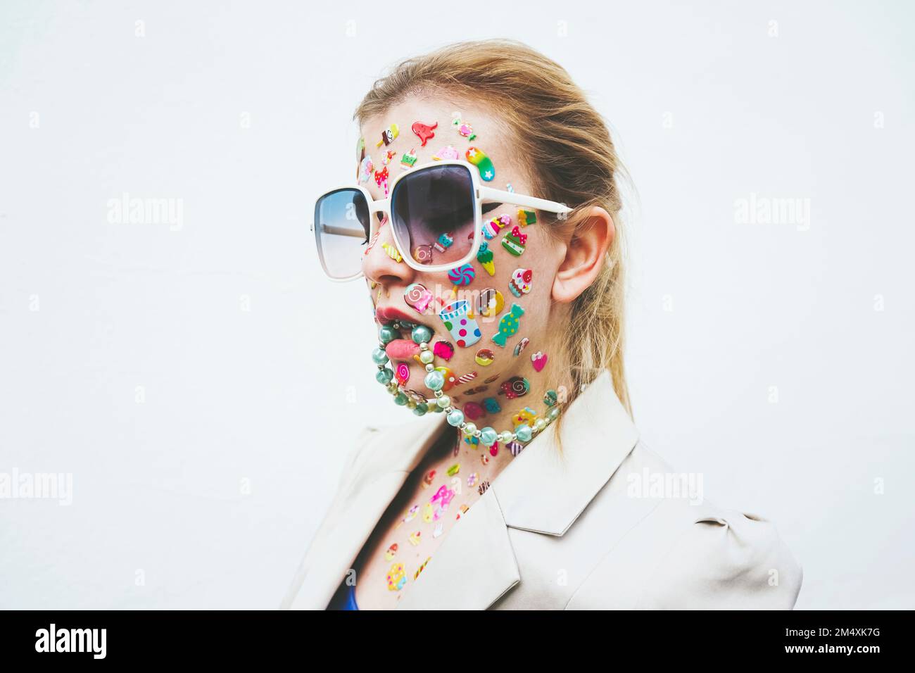 Femme avec des autocollants multicolores sur le visage et collier dans la bouche sur fond blanc Banque D'Images