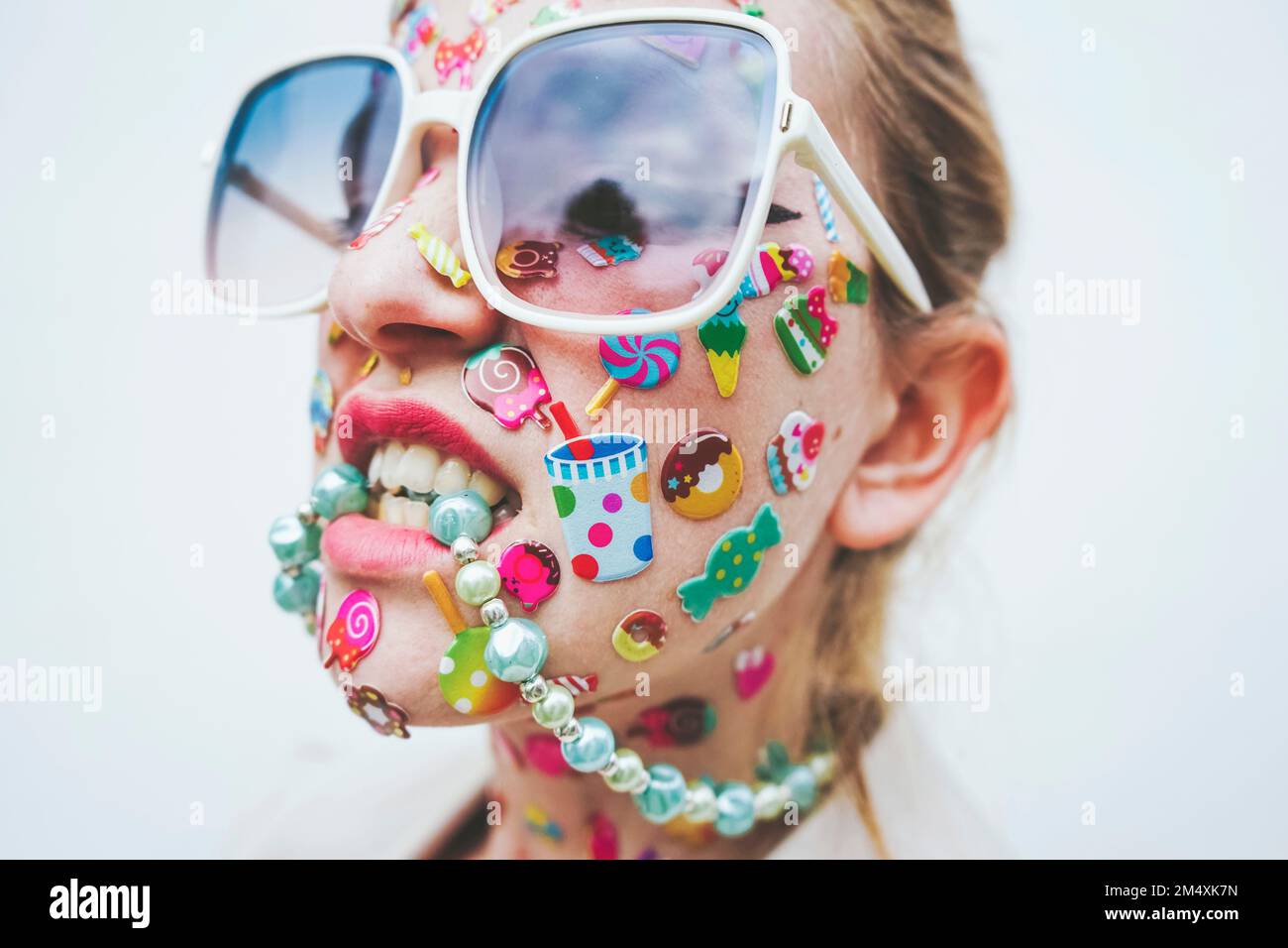 Femme avec des autocollants multicolores sur le visage collier mordant devant un fond blanc Banque D'Images