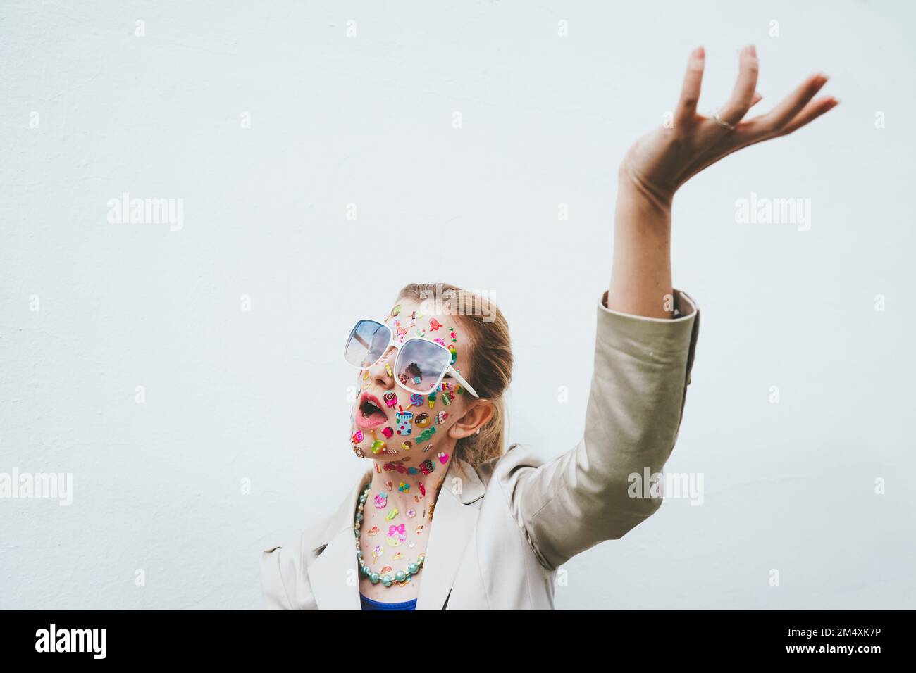 Femme avec des autocollants colorés sur le visage gestant devant un fond blanc Banque D'Images