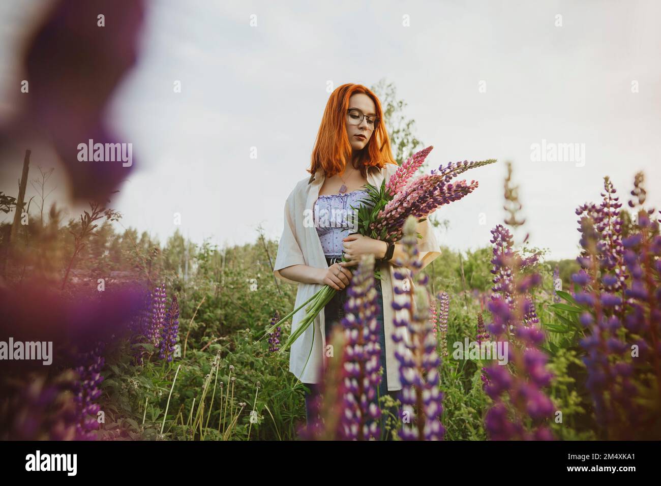 Adolescente debout avec des fleurs lupin sous le ciel Banque D'Images