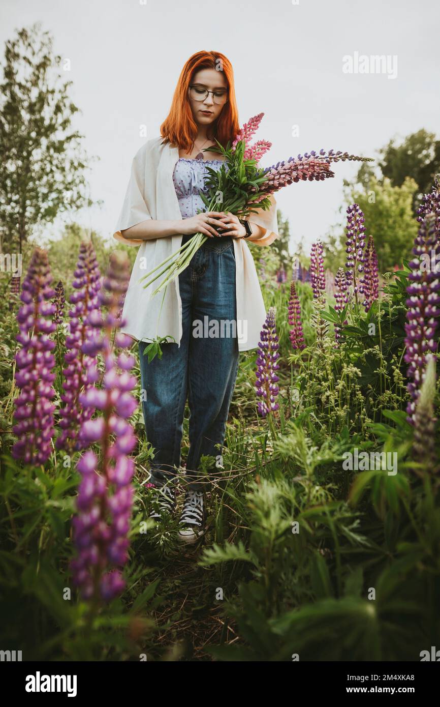 Adolescente marchant avec des fleurs lupin au champ Banque D'Images