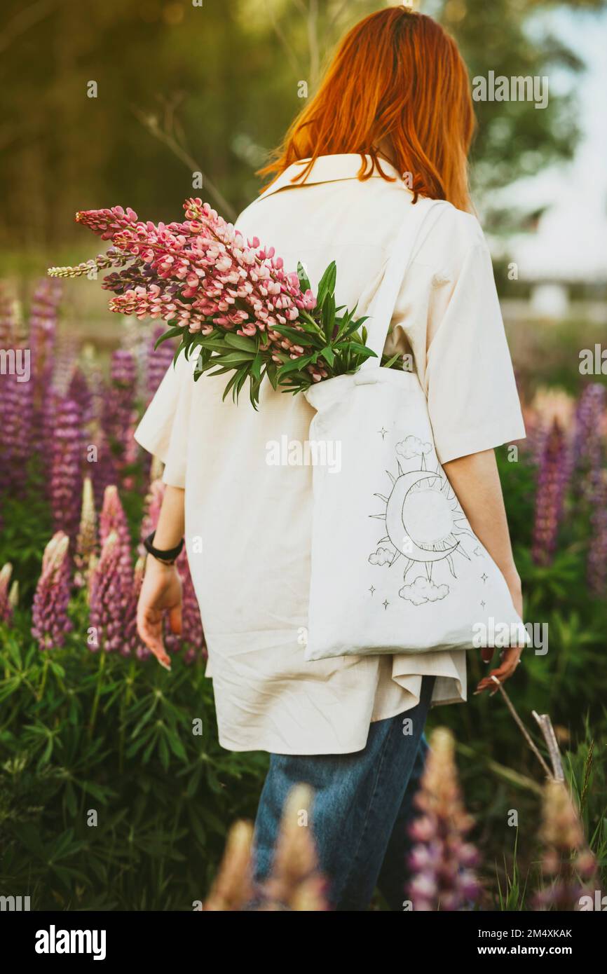 REDHEAD fille marchant avec des fleurs lupin dans un sac fourre-tout sur le terrain Banque D'Images