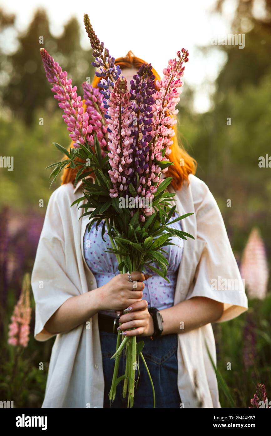 Adolescente couvrant le visage avec des fleurs lupin Banque D'Images