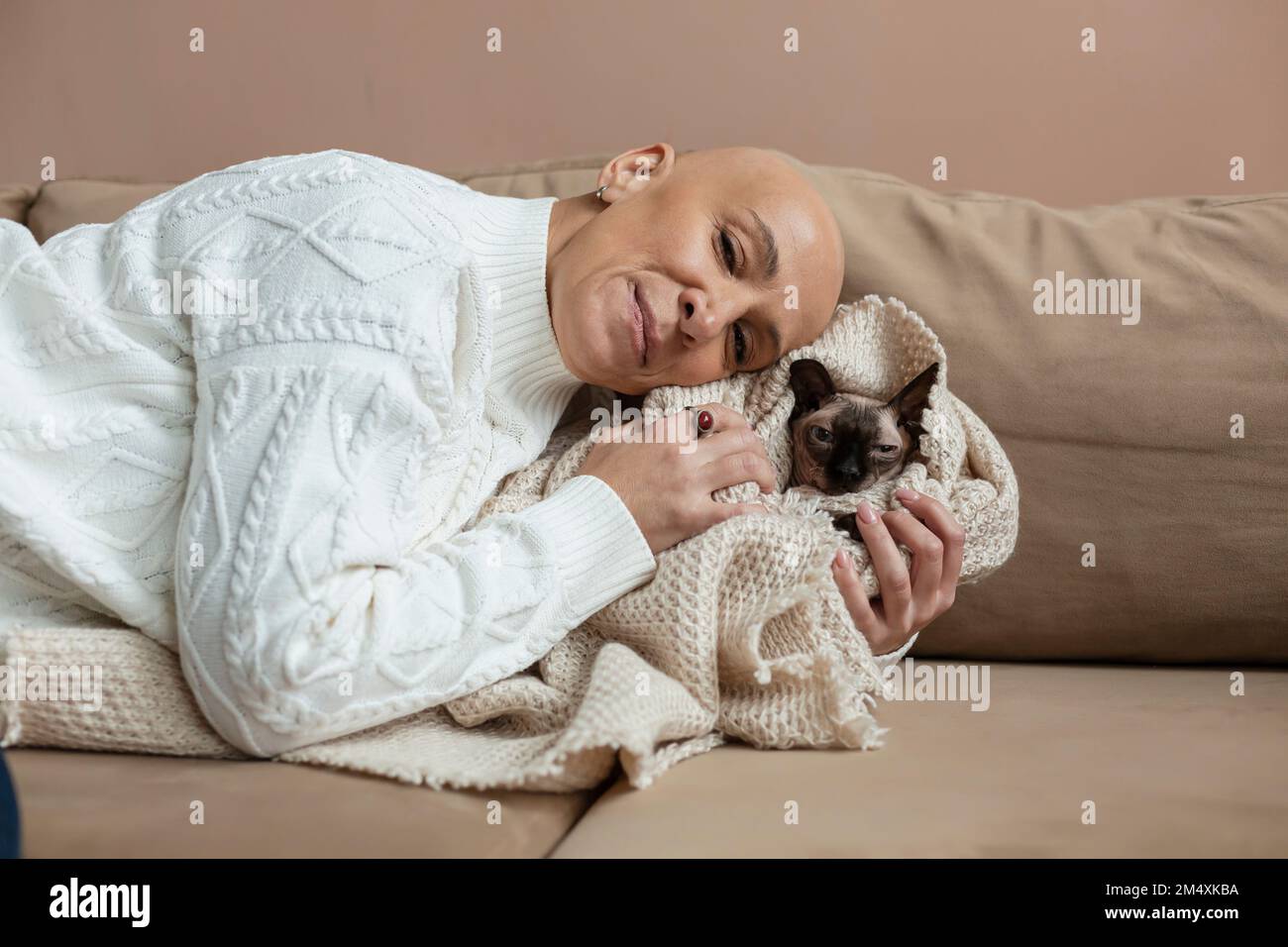 Femme chauve embrassant Sphynx chat enveloppé dans une couverture sur le canapé Banque D'Images