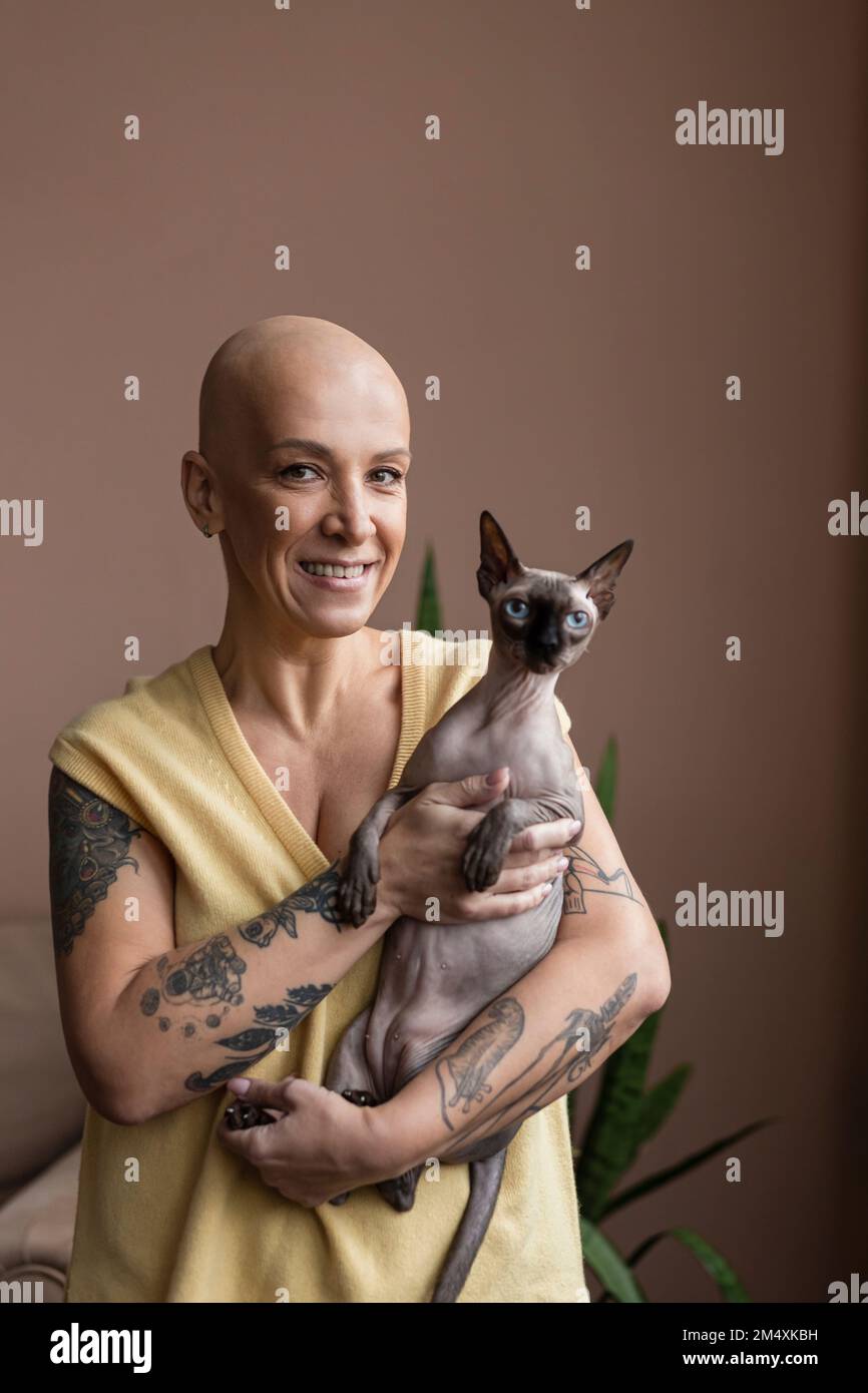 Femme chauve souriante portant un chat sans cheveux dans les bras Banque D'Images