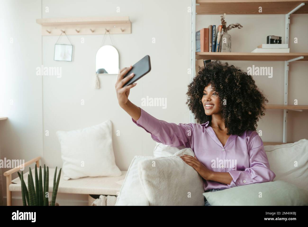 Femme souriante qui prend son selfie à la maison par téléphone portable Banque D'Images