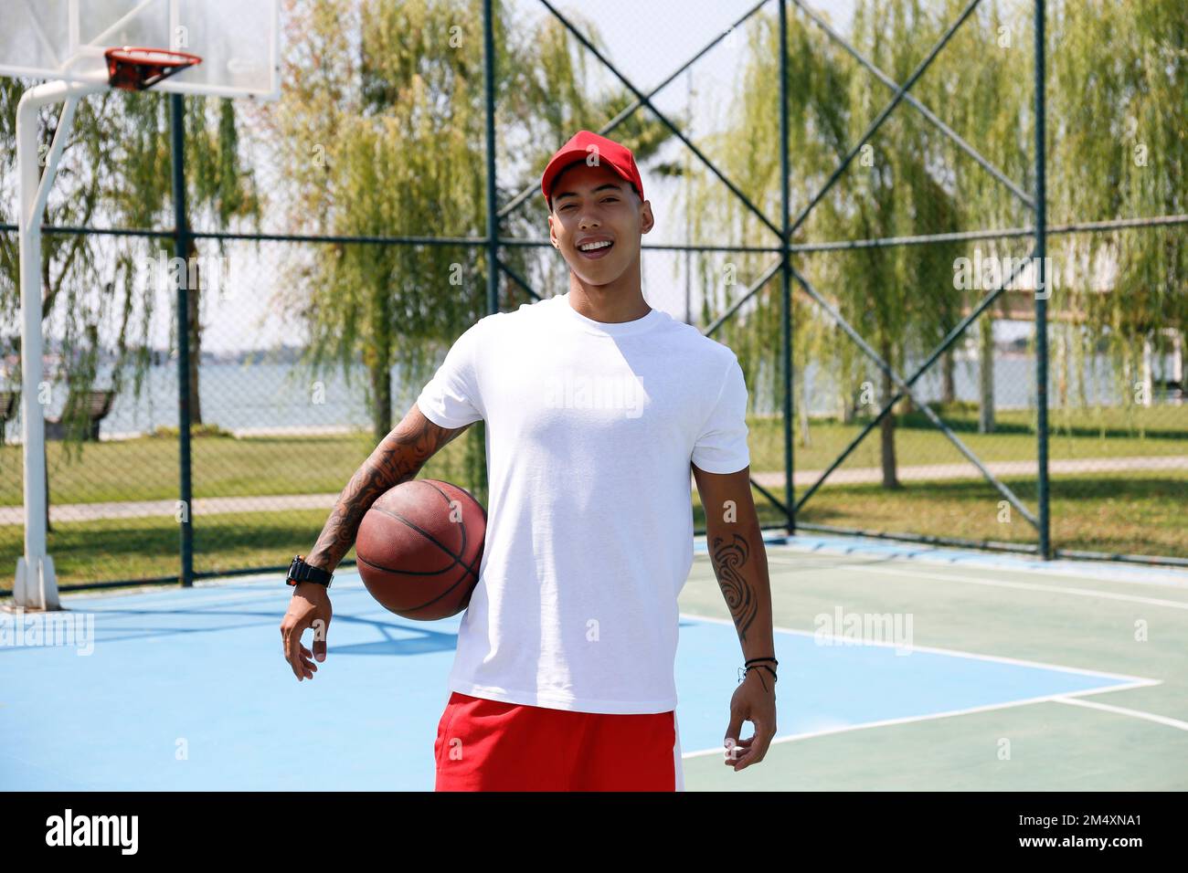 Homme souriant avec un ballon de basket debout sur un terrain de sport Banque D'Images