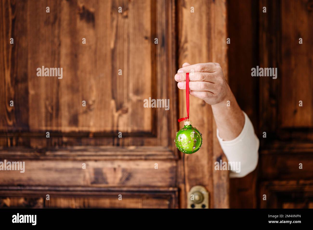 Main tenant la boule de Noël verte devant la porte en bois Banque D'Images